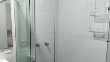 Une cabine de douche fermée par des parois de verre, avec un mur recouvert de carreaux blancs et un sol bleu.