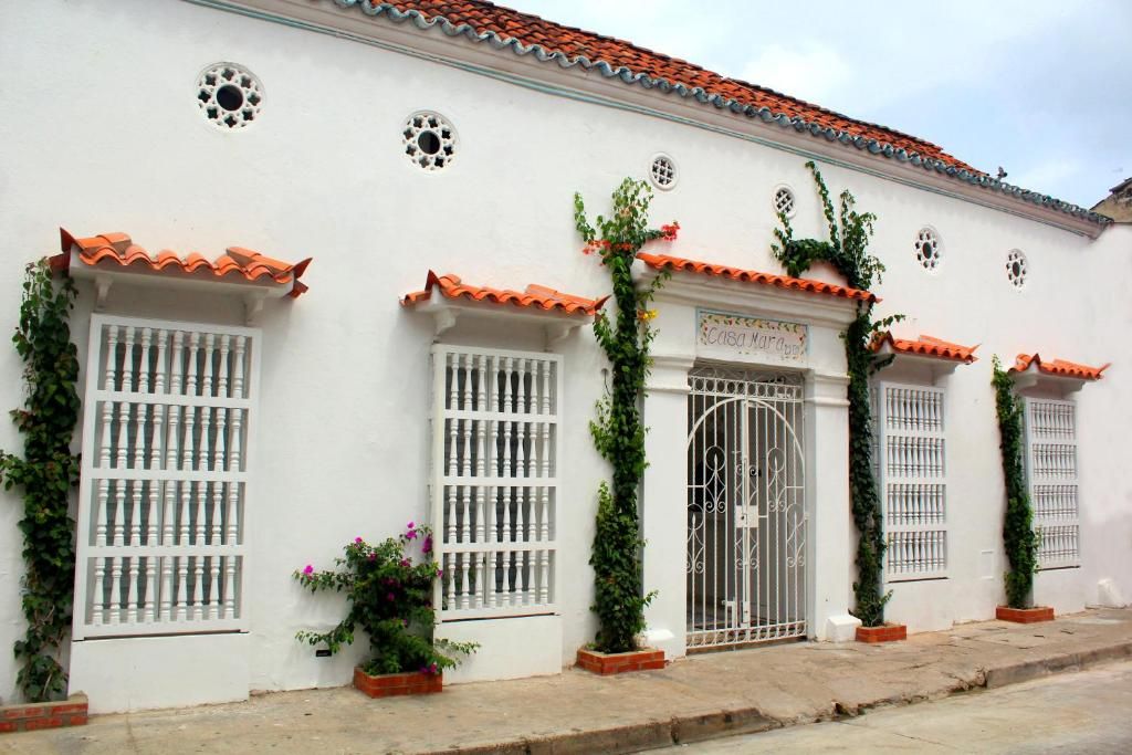 Un edificio blanco con tejados de tejas rojas, ventanas con barrotes y una entrada protegida por una reja.