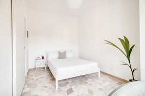 A bedroom with a white bed, a bedside table with a lamp, and a potted plant. - Hostmate- Milano-Minimal Nest (Milan)