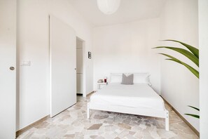 Quarto com piso estampado em pedra, cama branca e planta em vaso.