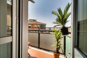 A balcony with a potted plant, a chair, and a view of buildings. - Hostmate- Milano-Minimal Nest (Milan)