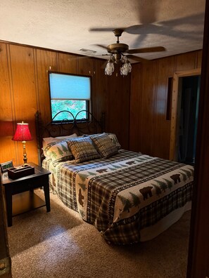 A bedroom with a bed, a nightstand, a lamp, a ceiling fan, and a window. - Cozy Mountain Cabin Retreat in Murphy, NC (Murphy)