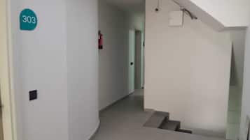Un pasillo con una escalera, un extintor y un cartel con un número en la pared.