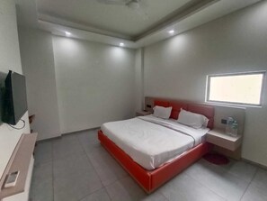 Quarto de hotel com cama, mesa de cabeceira, televisão e janela.