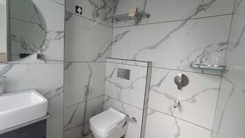 Un bany amb vàter blanc, un rentapeus i zona de dutxa.