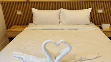 A hotel room with a bed, two pillows, a wooden headboard, and a heart-shaped towel arrangement.