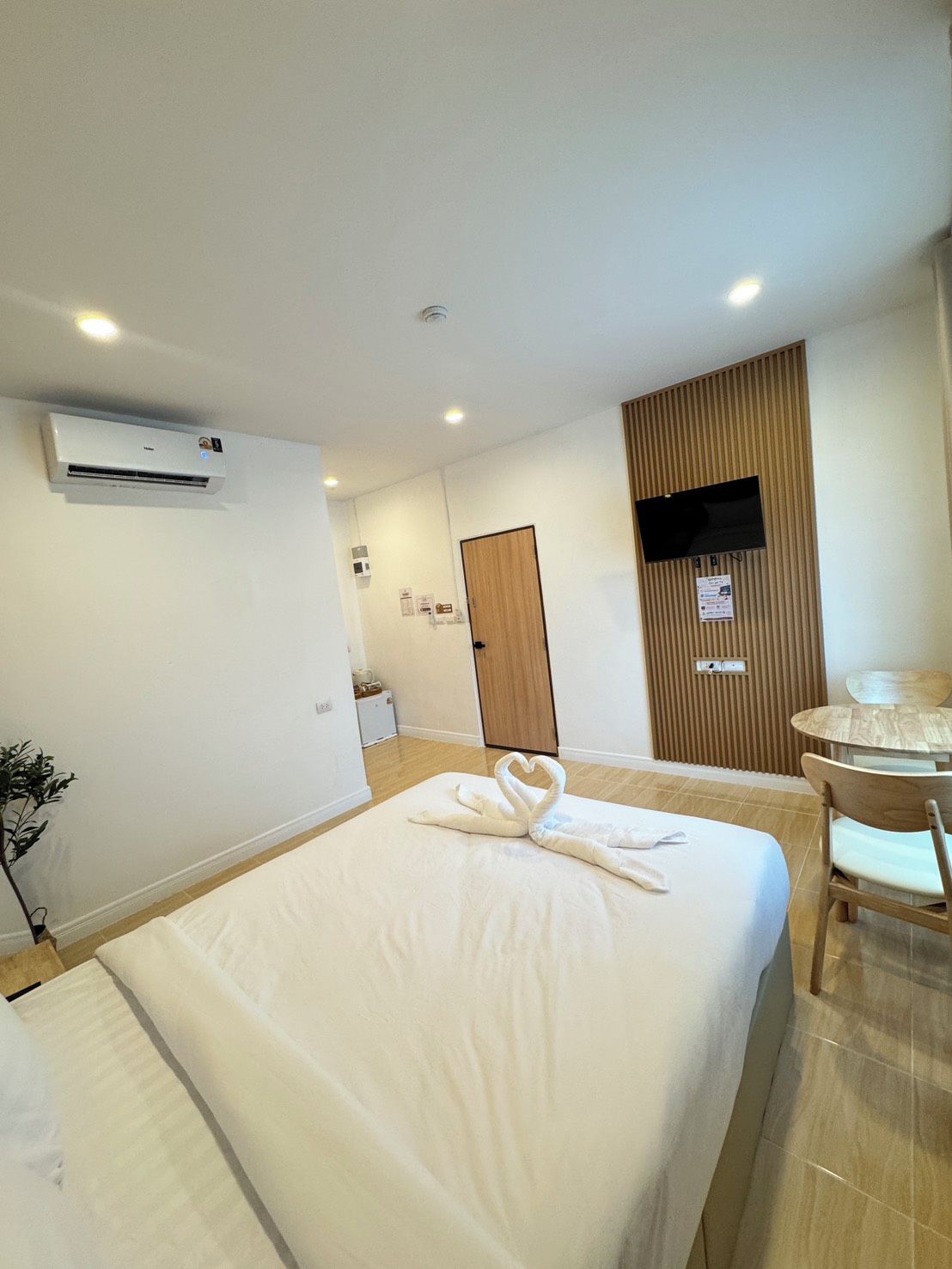 A hotel room with a bed, a desk, a chair, an air conditioning unit, and a television.