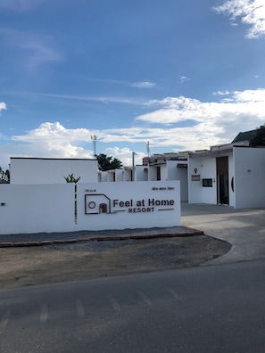 A sign for 'Feel at Home Resort' with a modern building in the background. - Feel at home resort  (Nakhon Pathom)