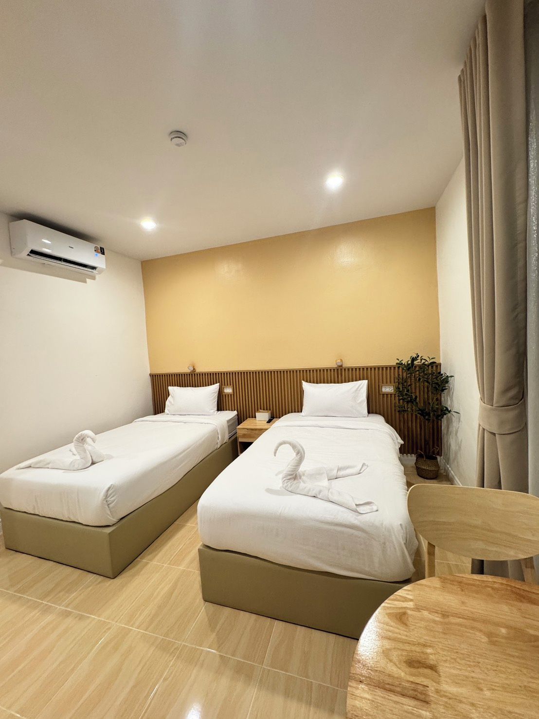Habitación de hotel con dos camas, una mesita, una silla, un equipo de aire acondicionado y una planta en maceta.