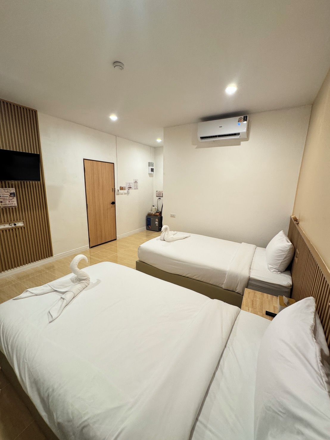 A hotel room with two beds, a wooden panel wall, an air conditioning unit, and a television.