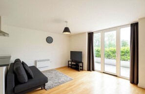 A modern living room with a sofa, a flat-screen TV, and a large sliding glass door leading to an outdoor area. - Tranquil 1-bedroom apartment in the heart of London right next to the riverside (London)