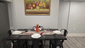 Ein Essbereich mit einem Tisch für vier Personen, Stühlen, einem Bild an der Wand und einer Vase mit Obst.