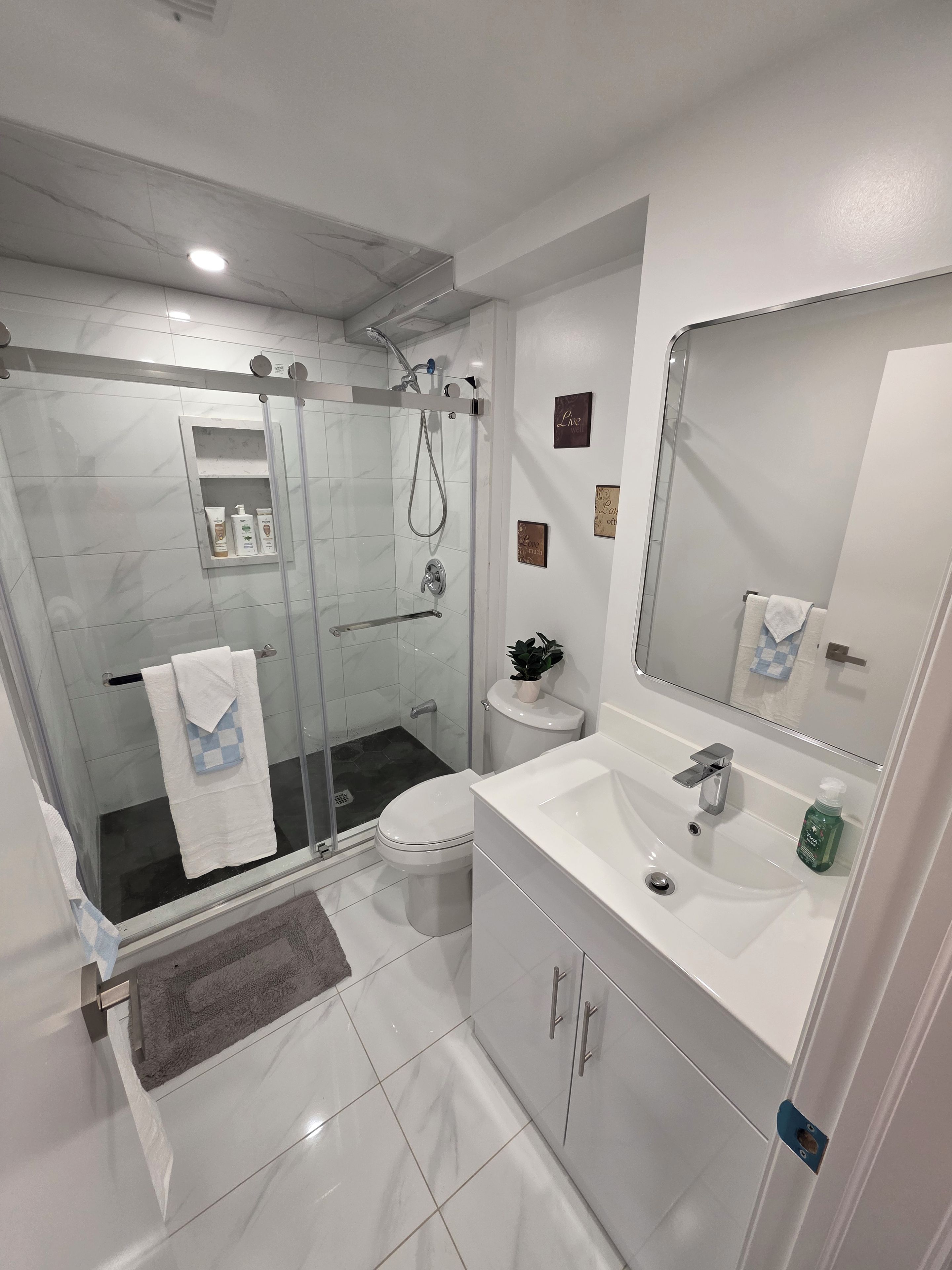 A modern bathroom with a glass-enclosed shower, a white sink, and a large mirror.