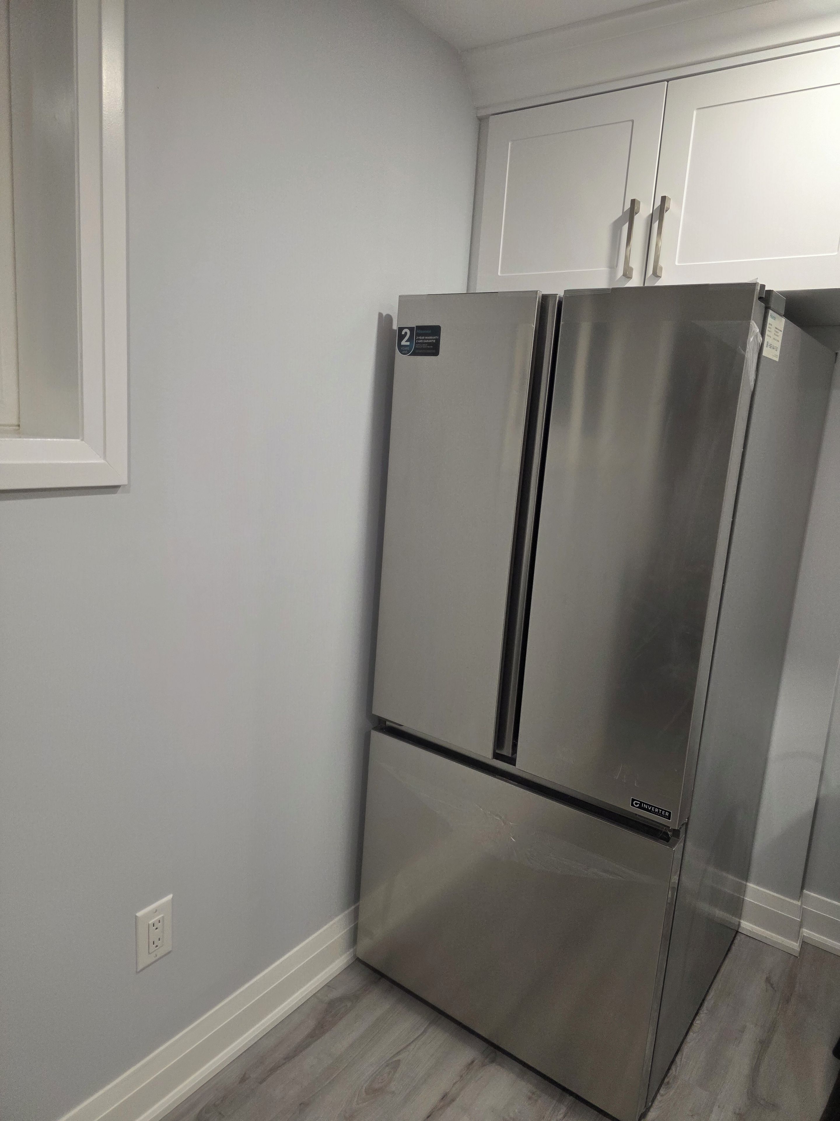 Un réfrigérateur en acier inoxydable dans une cuisine aux murs de couleur gris clair et au plancher en bois.