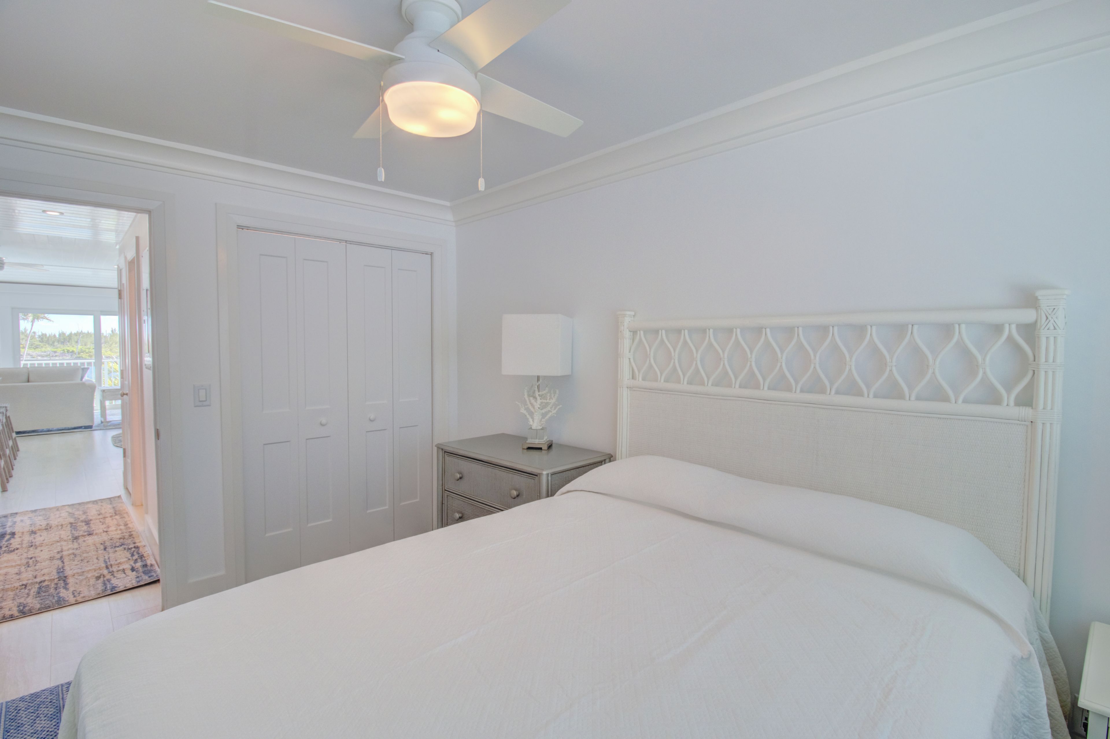 Une chambre à coucher comprenant un lit, une table de chevet, un ventilateur de plafond et une porte donnant sur un balcon.