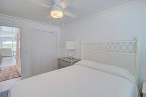 Ein Schlafzimmer mit einem Bett, einem Nachttisch, einem Deckenventilator und einer Tür, die auf einen Balkon führt.