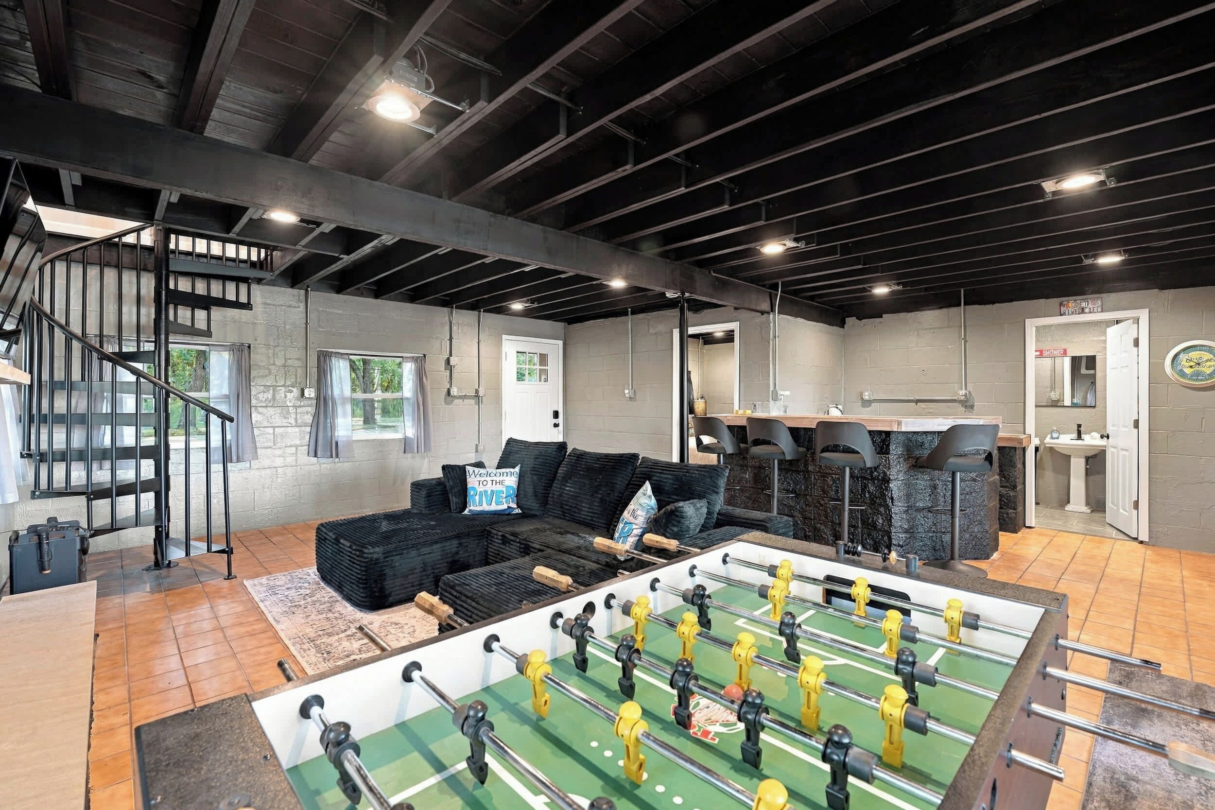A spacious room with a foosball table, a sofa, and a staircase.