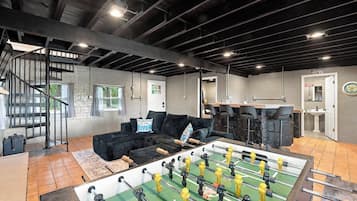 A spacious room with a foosball table, a sofa, and a staircase.