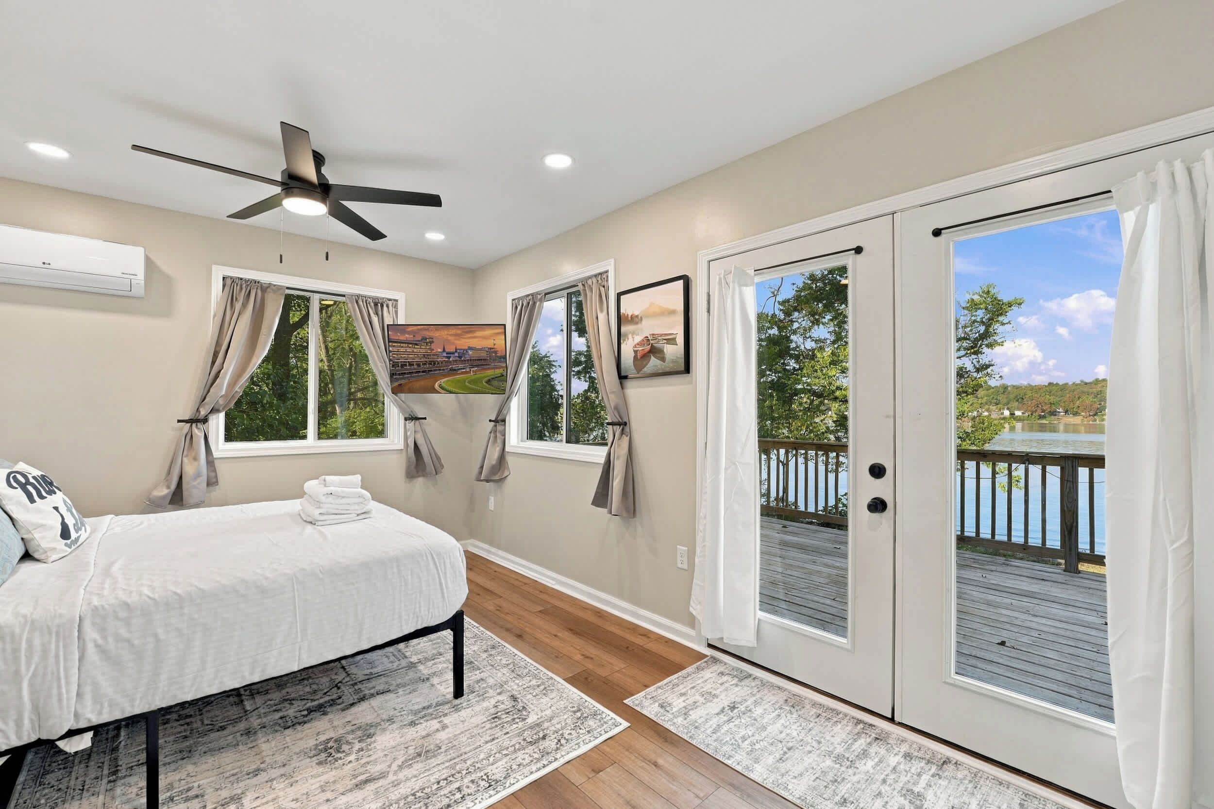 A bedroom with a bed, a ceiling fan, a large window, and a view of a lake.