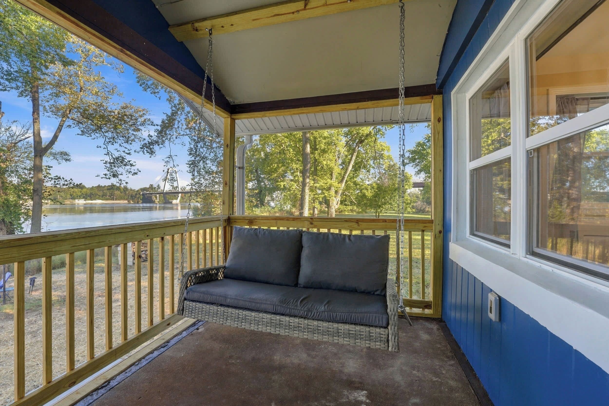 Un porche techado con un asiento mecedora, vista a un lago y una terraza de madera.