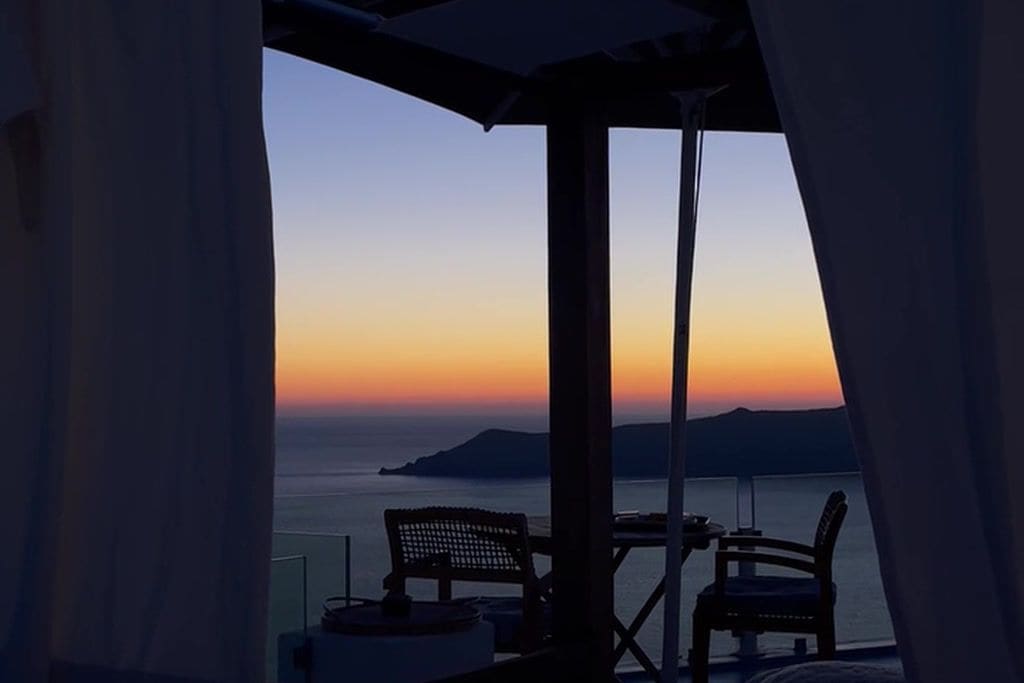 A balcony with a view of the sea at sunset, featuring a table and two chairs.