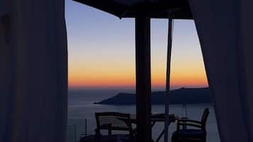 A balcony with a view of the sea at sunset, featuring a table and two chairs.