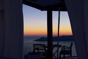 Ein Balkon mit Blick auf das Meer bei Sonnenuntergang, ausgestattet mit einem Tisch und zwei Stühlen.