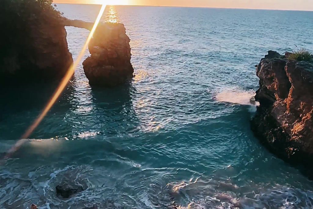A coastal scene with clear water, rocky formations, and sunlight reflecting off the surface.
