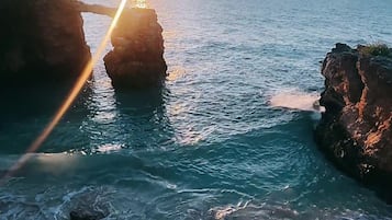A coastal scene with clear water, rocky formations, and sunlight reflecting off the surface.