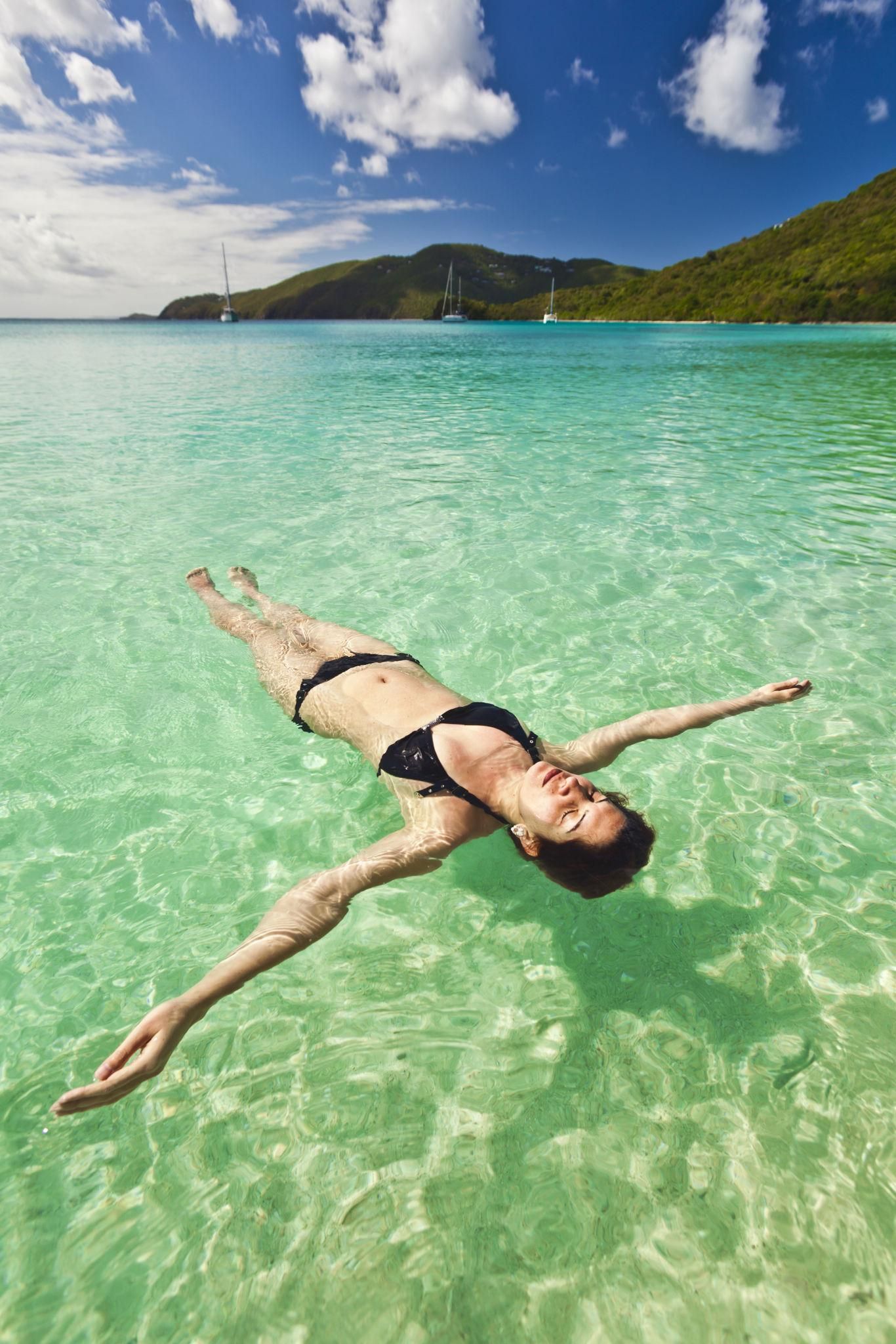 A person floating in clear turquoise water with a mountainous landscape in the background.