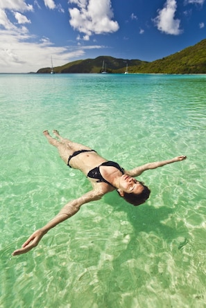 A person floating in clear turquoise water with a mountainous landscape in the background.