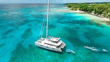 A sailboat anchored in clear turquoise waters with a beach and greenery in the background.