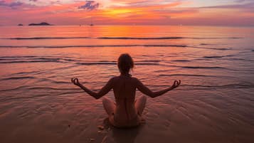 A person sitting on a beach facing the ocean at sunset.