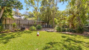 A backyard with a grassy lawn, a dog, and a wooden fence. - Coolangatta Dreaming - Pet Friendly Beachside Home - Min. 2 Night Stays (Coolangatta)