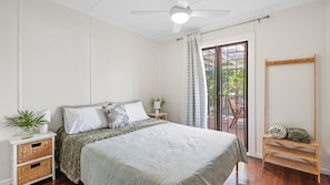 Ein Schlafzimmer mit einem Bett, Nachttischen, einem Deckenventilator, einem Fenster mit Vorhängen und einem Holzsessel.