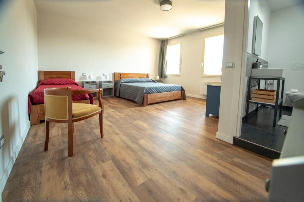 A bedroom with two beds, a chair, a desk, and a bathroom area.