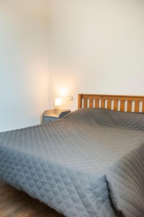A bed with a wooden headboard, a nightstand with a lamp, and a plain wall. - FORESTERIA LOMBARDA BED AND BIKE CREMONA (Crotta d'Adda)