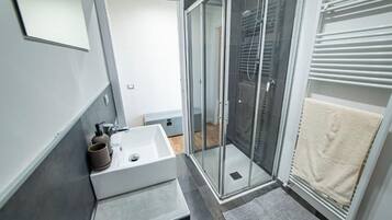 Un bany modern amb una dutxa de vidre, un lavabo blanc i un escurapulides.
