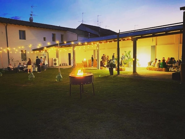 An outdoor gathering area with a fire pit, covered seating, and string lights.
