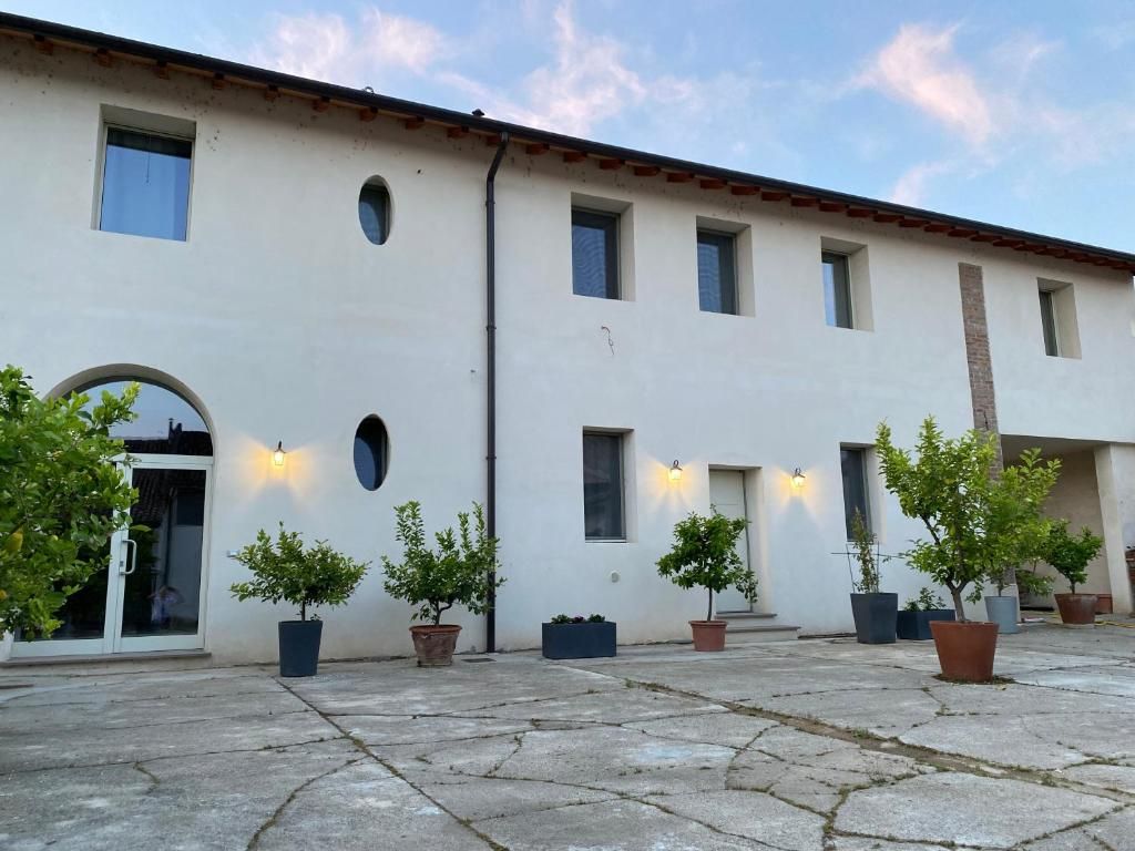 Edifici amb façana blanca, nombroses finestres i un pati empedrat amb plantes en testos.