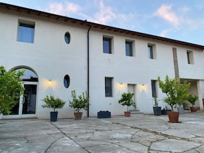 A building with a white facade, multiple windows, and a paved courtyard with potted plants.