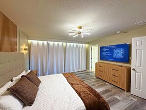 Quarto de hotel com cama, televisão, ventoinha no teto e porta.