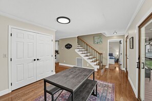 A spacious hallway with a wooden floor, a dining area with a table and benches, a staircase with a wooden handrail, and a kitchen area in the background. - Hap’s Sweet Hideaway | Lakefront Cabin & Dock (Maynardville)