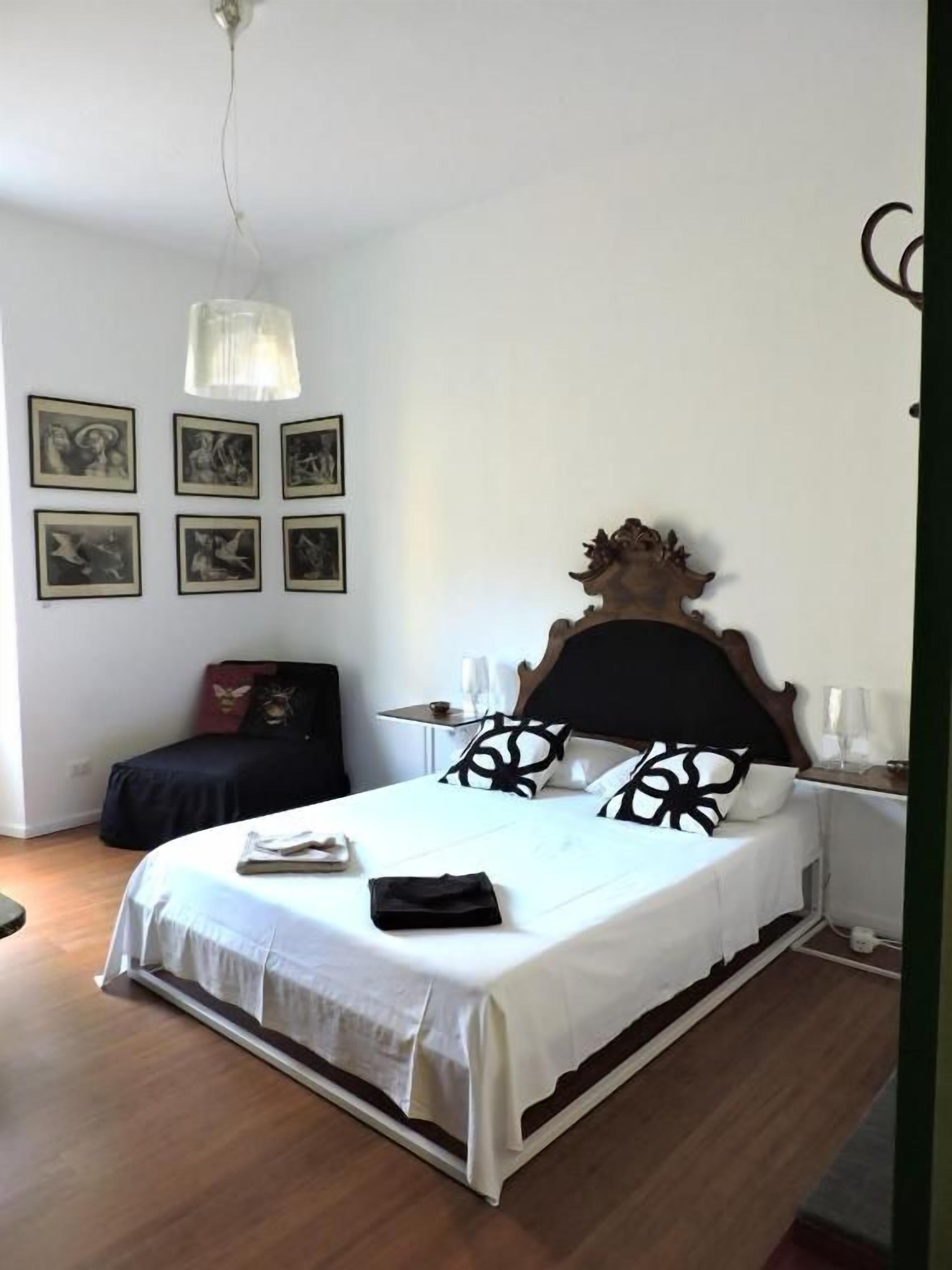 Un dormitorio con una cama, mesitas de noche, una lámpara colgante y cuadros en la pared.