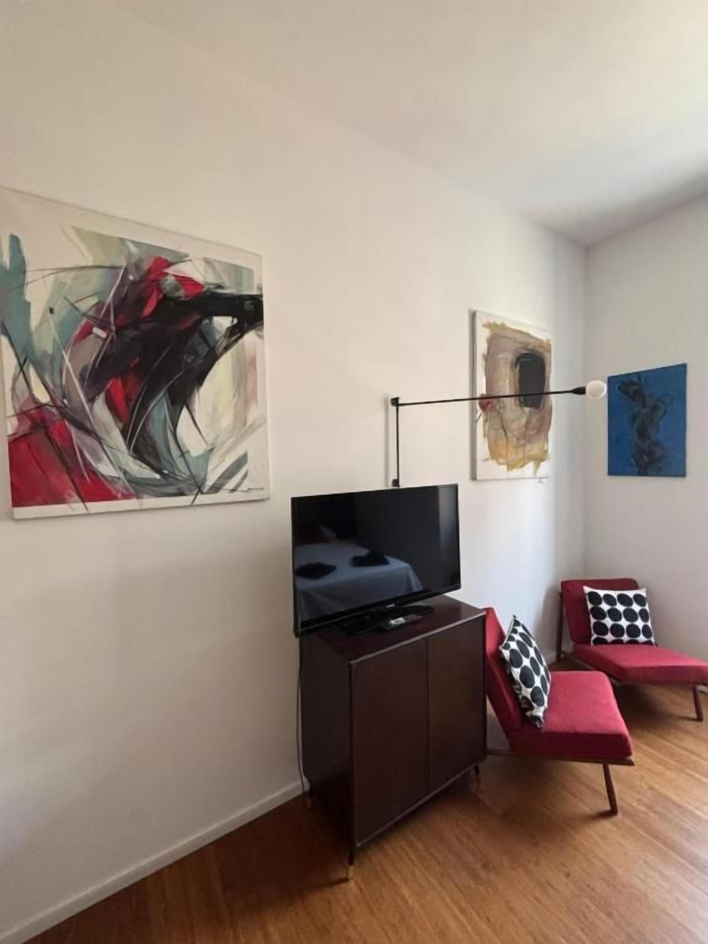 A modern living room with a flat-screen TV, a dark wooden cabinet, a red sofa, and abstract wall art.