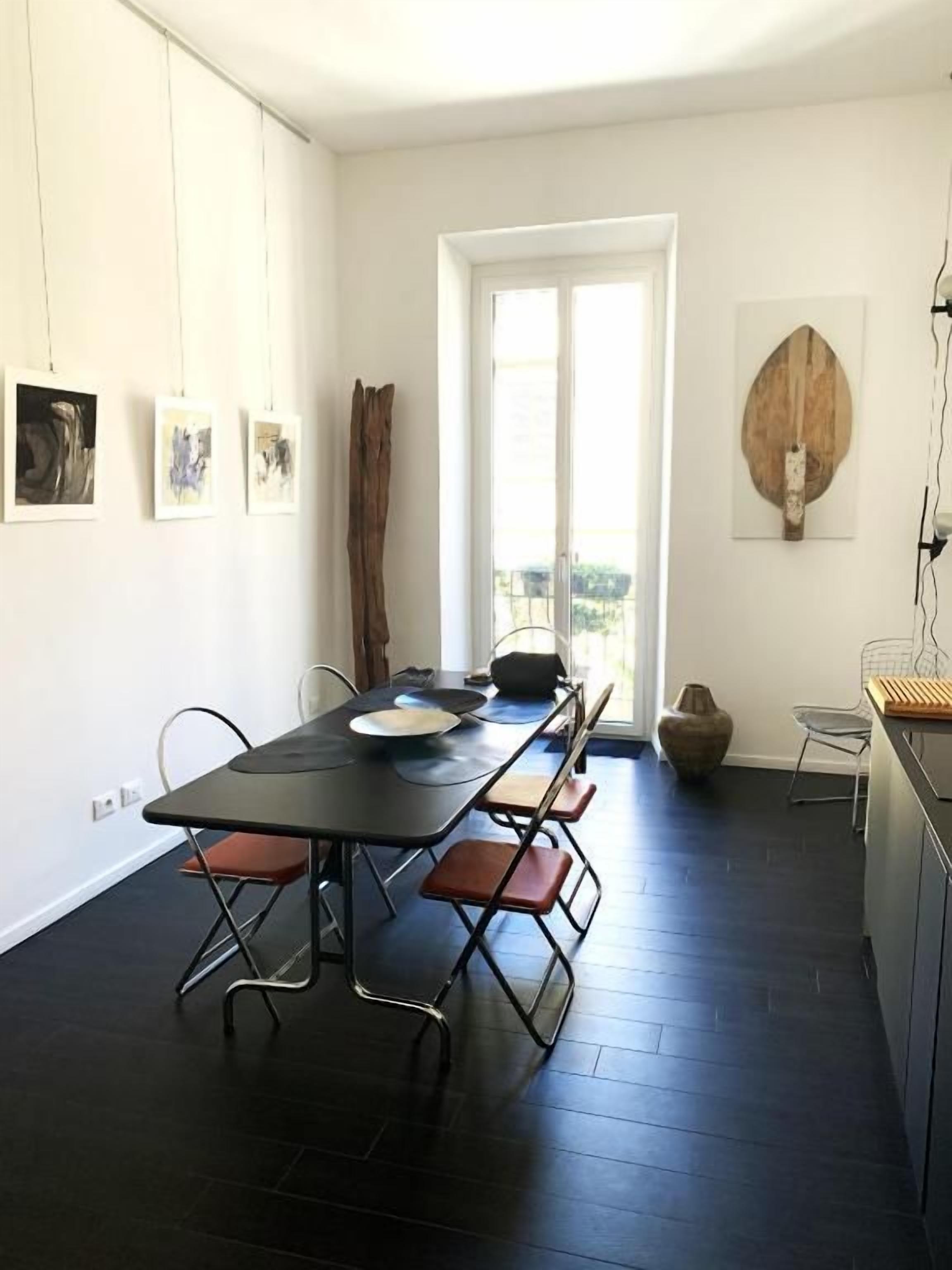 Un coin repas avec une table et des chaises noires, une porte blanche et une vue à travers la porte.