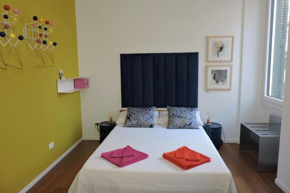 Ein Hotelzimmer mit Bett, Nachttisch, Fenster und Wanddekoration.
