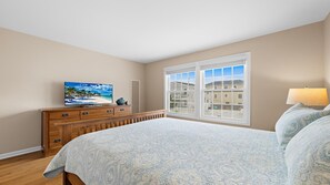 A bedroom with a large bed, a dresser, a television, and a window with a view of buildings. - Beautiful 5 Bedroom Home with a pool in Holgate! (Beach Haven)