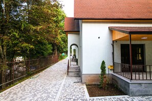 A building with a brick pathway leading to a gated entrance, surrounded by trees.