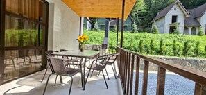 A balcony with a table and chairs, a wooden pergola, and a view of a house and greenery. - Jan In Dilijan: 2-Story 2-Bedroom Forest Cottage with BBQ #3 (Dilijan)